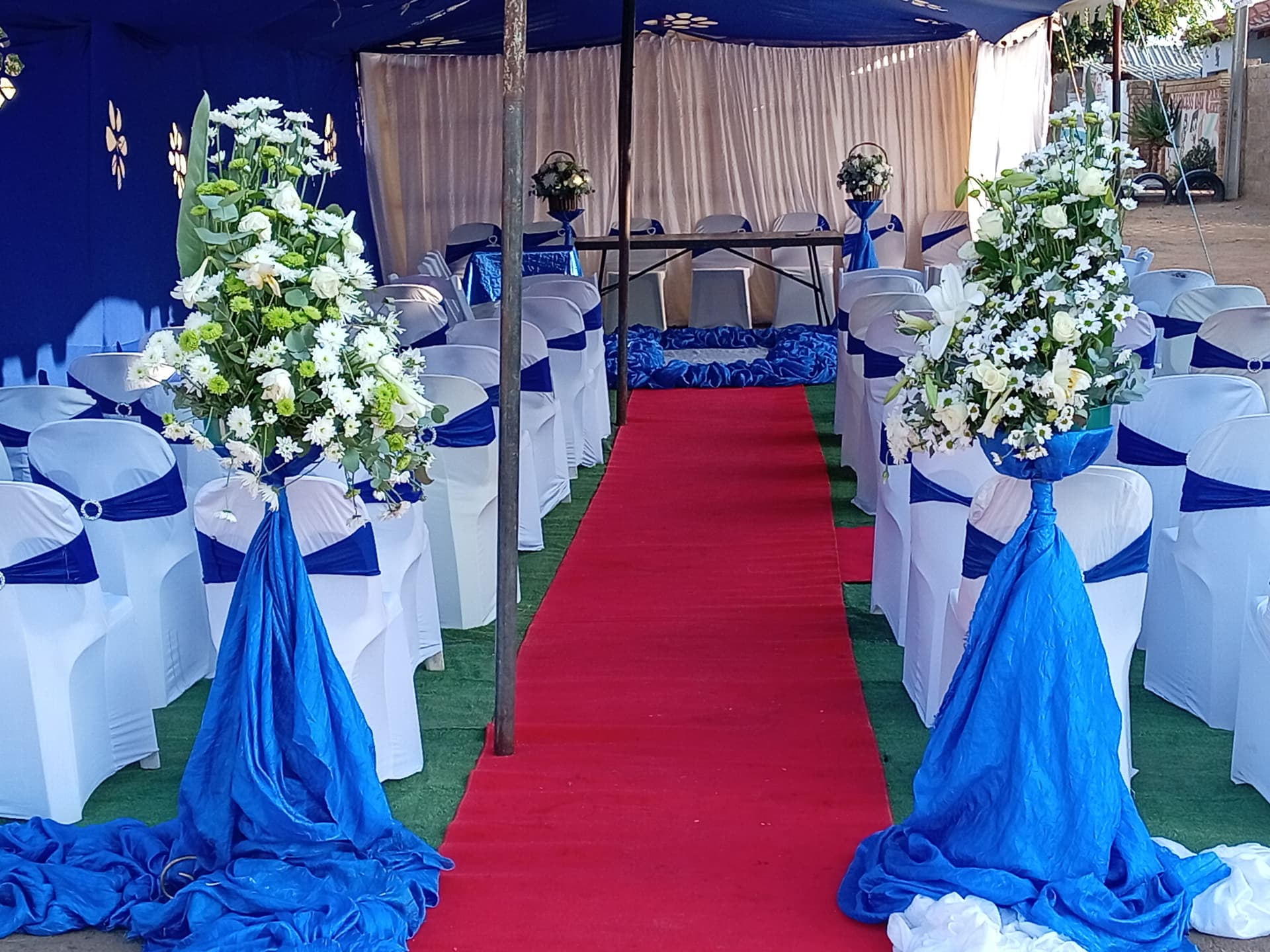 Aisle lined with fresh flower arrangements inside a draped tent